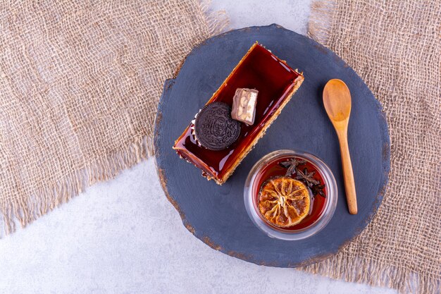 Rebanada de pastel, vaso de té y cuchara en tablero oscuro. Foto de alta calidad