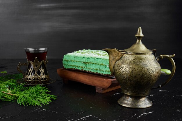 Una rebanada de pastel verde con un vaso de té.