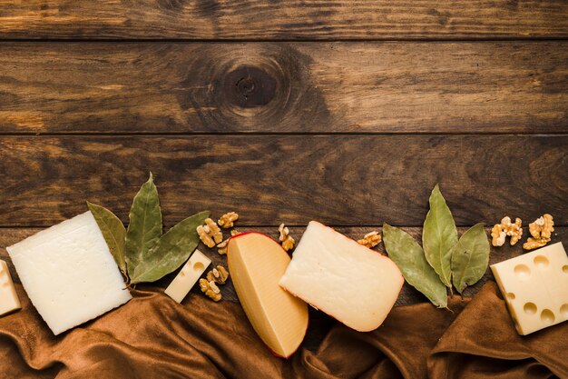 Rebanada de queso; Hojas de laurel y nogal colocan en la parte inferior del fondo de madera con material textil de seda