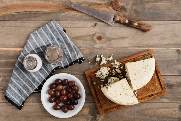 Foto gratuita rebanada de queso roquefort; aceitunas con salero y pimentero en mesa de madera
