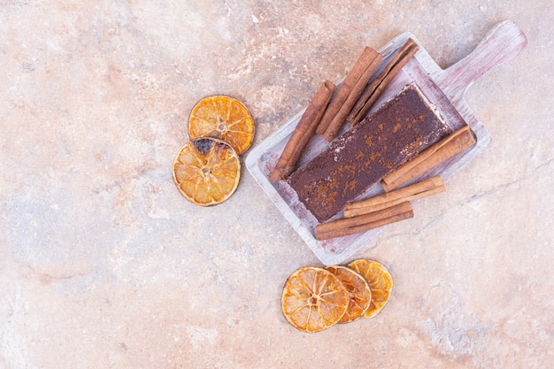 Foto gratuita una rebanada de tarta de chocolate en bandeja negra con ramitas de canela y rodajas de naranja secas.
