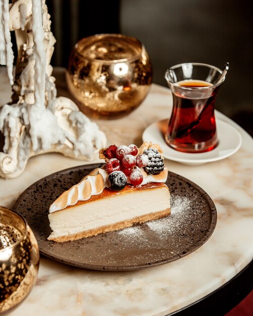 Rebanada de tarta de queso adornada con bayas servida con té negro