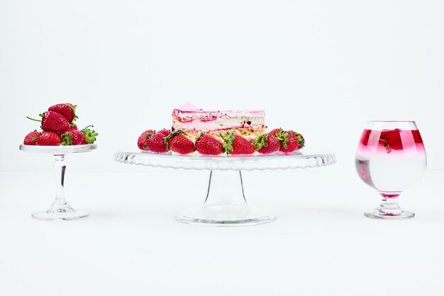 Una rebanada de tarta de queso de fresa con frutas y un vaso de bebida.