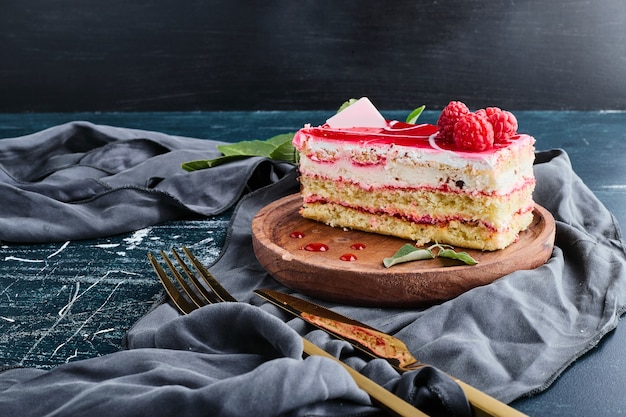 Rebanada de tarta de queso con jarabe de frambuesa aislado sobre fondo azul en una bandeja de madera.