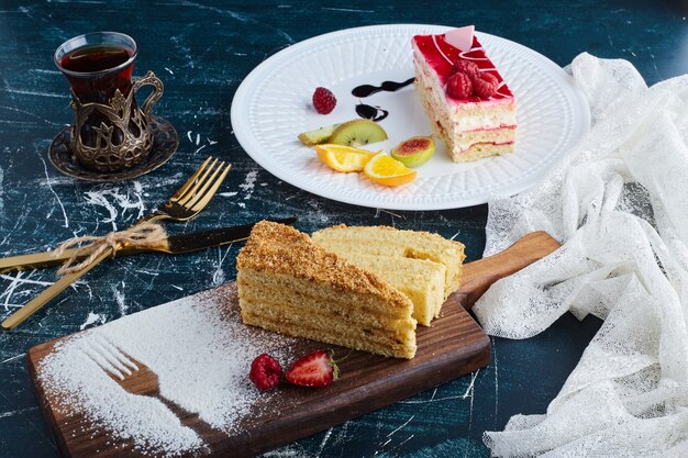 Rebanada de tarta de queso con jarabe de frambuesa en un plato blanco con un vaso de té.