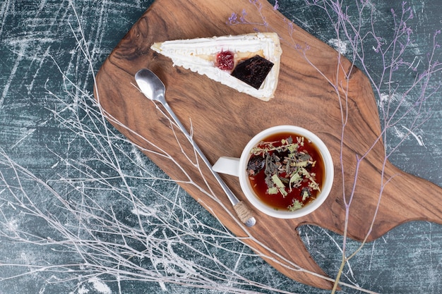 Rebanada de tarta de queso sobre tabla de madera con taza de té. Foto de alta calidad