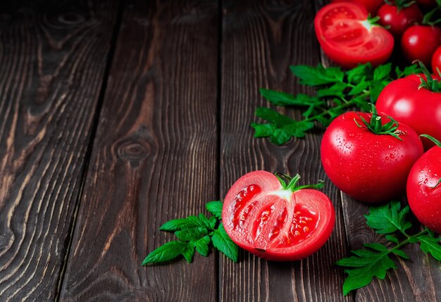 Rebanada de tomate y tomates rojos maduros de cerca sobre una superficie rústica oscura