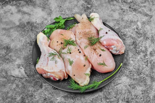 Rebanadas de carne de pollo cruda en placa negra con verduras picadas.