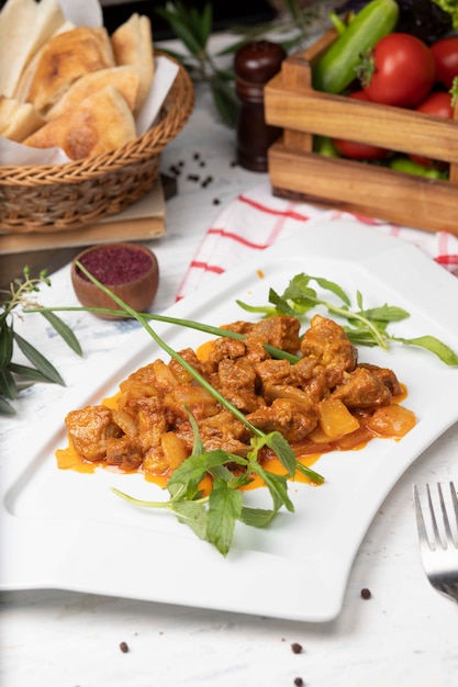 Rebanadas de carne de res guisadas en salsa de tomate con cebolla y pimientos. Servido en plato blanco con basilico.