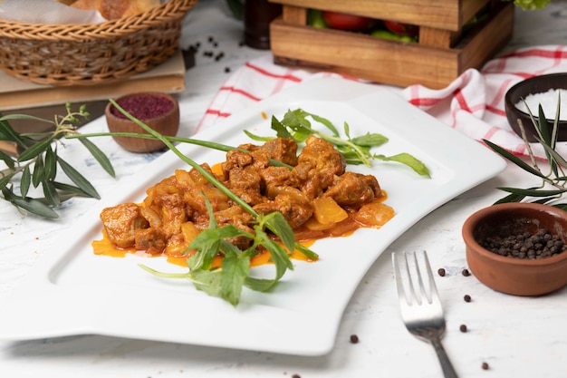 Rebanadas de carne de res guisadas en salsa de tomate con cebolla y pimientos. Servido en plato blanco con pimienta basílica, negra.