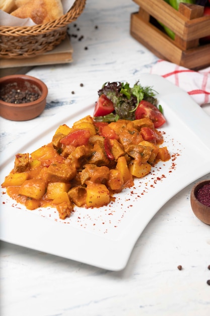 Rebanadas de carne de res guisadas en salsa de tomate con cebolla y pimientos. Servido en plato blanco con pimienta basílica, negra.