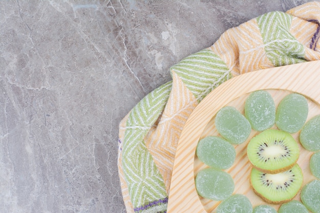 Rebanadas de kiwi y dulces de mermelada en placa de madera.