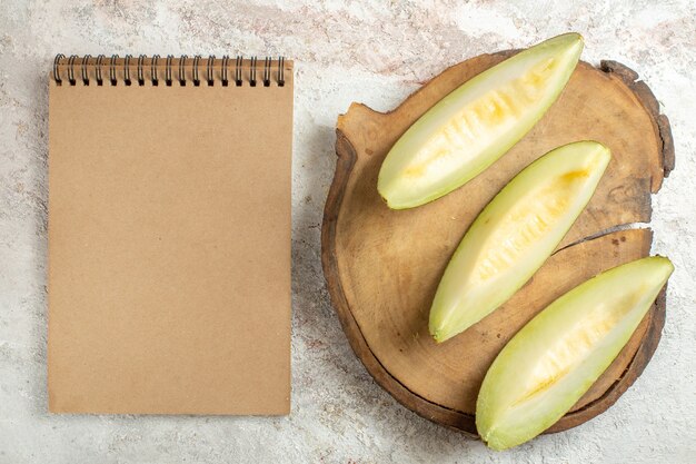 Rebanadas de melón en bandeja de madera y cuaderno de mármol blanco