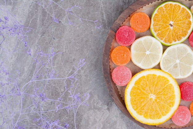 Rebanadas de naranja, limón y caramelos en placa de madera.