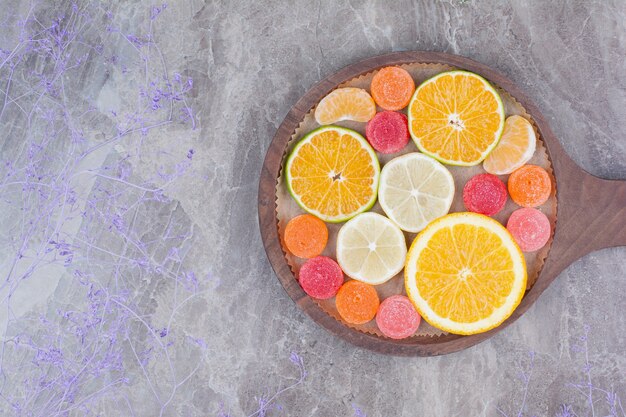 Rebanadas de naranja, mandarina y caramelos en tabla de cortar.