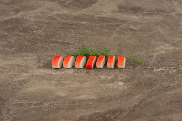 Rebanadas de palitos de cangrejo con verduras en la mesa de mármol.