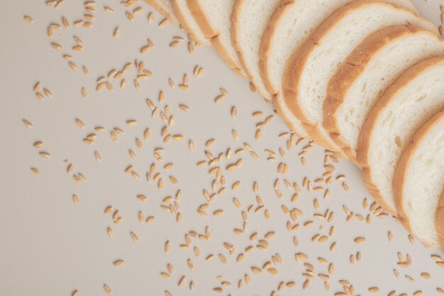 Rebanadas de pan blanco fresco con granos de avena sobre superficie blanca