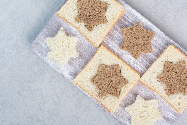 Rebanadas de pan blanco y negro en forma de estrella y cuadrado sobre placa de madera. Foto de alta calidad