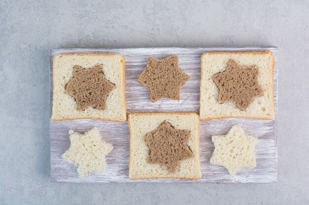 Rebanadas de pan blanco y negro en forma de estrella y cuadrado sobre placa de madera