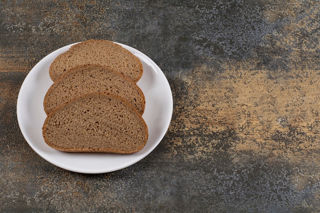 Rebanadas de pan de centeno negro en la placa blanca.