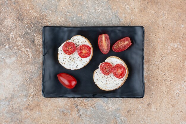 Rebanadas de pan con crema y tomate en placa negra