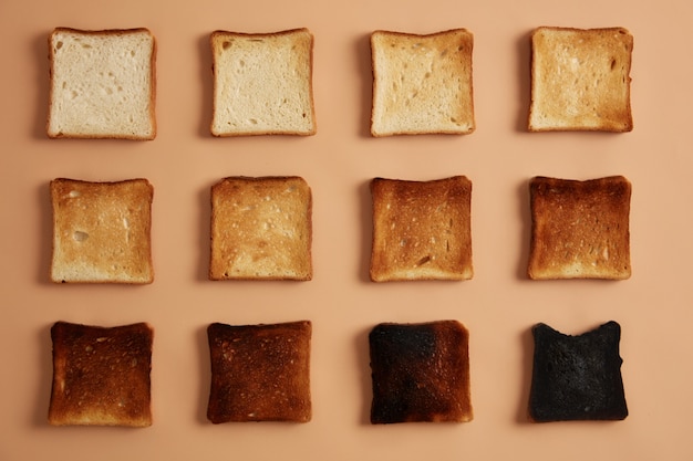 Rebanadas de pan de diversos grados de tostado dispuestas en filas sobre un fondo beige. Tostadas o bocadillos para comer. Etapas de tostado. Concepto de alimentación, bocadillos y dieta saludable. Foto de estudio