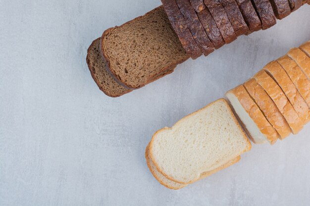 Foto gratuita rebanadas de pan fresco blanco y marrón sobre fondo de mármol.