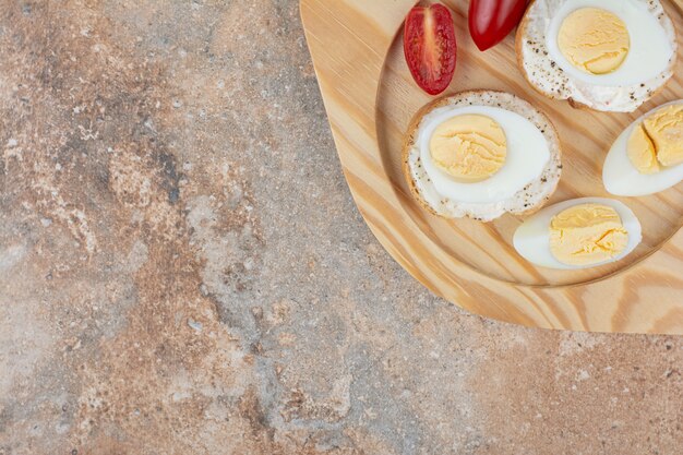 Rebanadas de pan con huevos duros y tomate en placa de madera