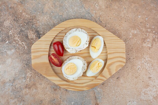 Rebanadas de pan con huevos y tomates cocidos en placa de madera