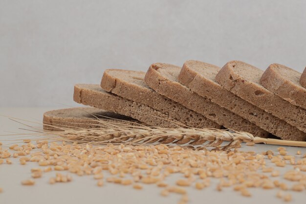 Rebanadas de pan integral fresco con granos de avena sobre superficie blanca