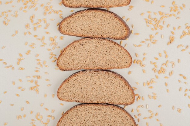 Rebanadas de pan integral fresco con granos de avena sobre superficie blanca