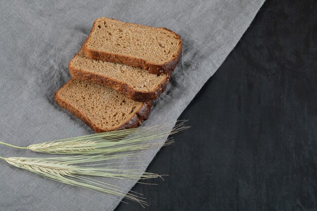 Rebanadas de pan integral con trigo sobre un mantel gris.