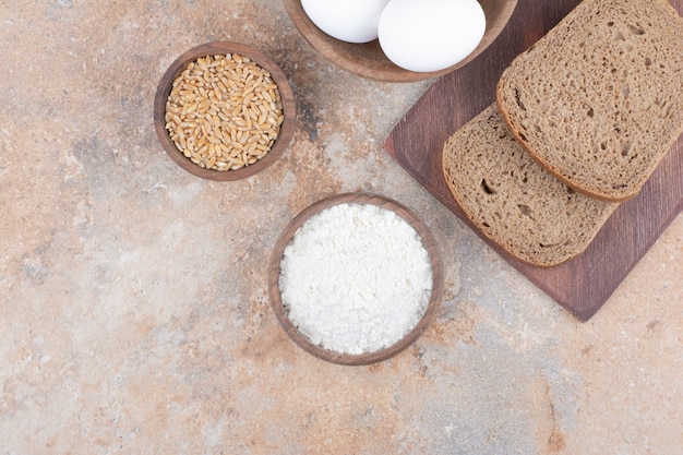 Rebanadas de pan negro, harina, cebada y huevos sobre superficie de mármol