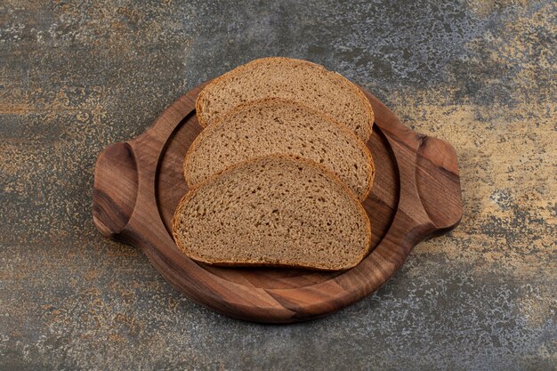 Rebanadas de pan negro sabroso sobre tabla de madera.