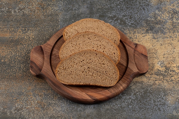 Rebanadas de pan negro sabroso sobre tabla de madera.