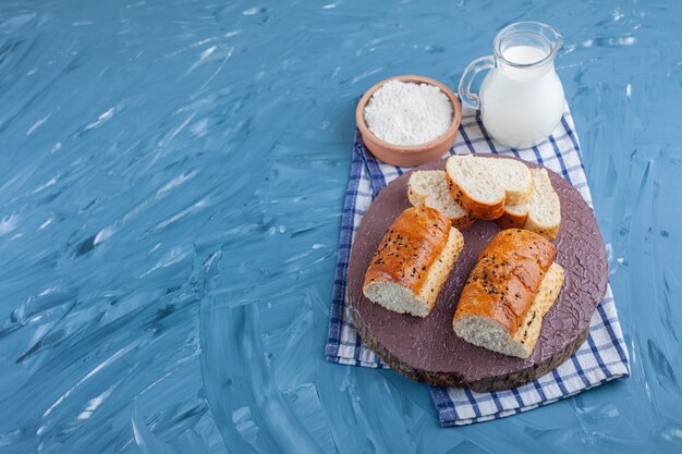 Rebanadas de pan en una tabla junto a un huevo cocido y un cuenco de harina sobre una toalla, sobre la mesa azul.