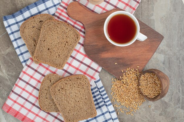 Rebanadas de pan y taza de té sobre manteles con cebada. Foto de alta calidad