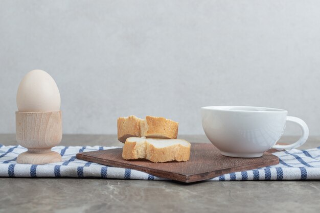 Rebanadas de pan y taza de té sobre tabla de madera con huevo. Foto de alta calidad