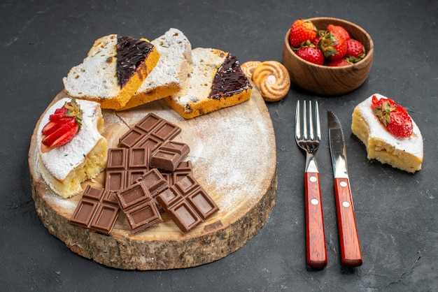 Rebanadas de pastel de vista frontal con barras de chocolate y fresas sobre fondo gris