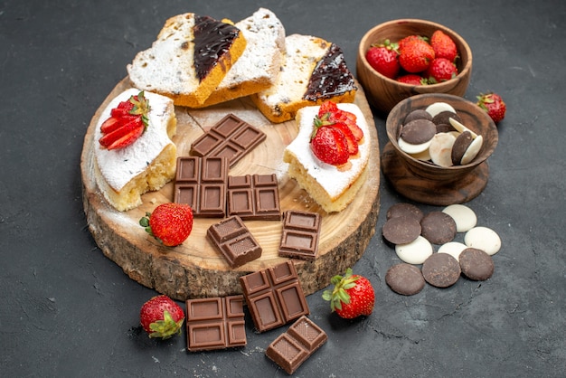 Rebanadas de pastel de vista frontal con barras de chocolate y galletas sobre fondo oscuro