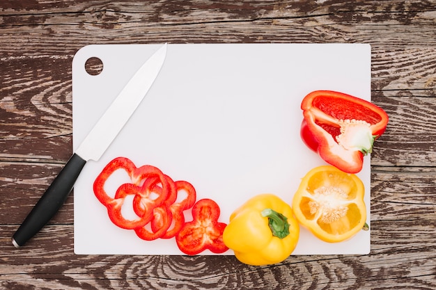 Rebanadas de pimientos rojos con cuchillo afilado en tablero blanco sobre la mesa de madera