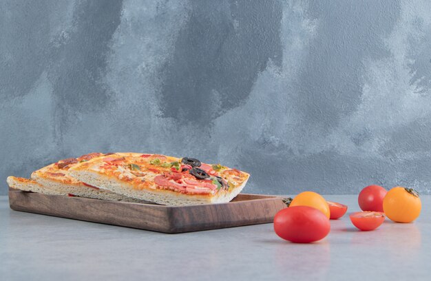 Foto gratuita rebanadas de pizza en una bandeja junto a pequeños tomates en mármol