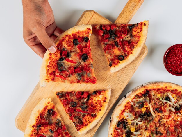 Rebanadas de pizza con especias en un tablero de pizza sobre fondo blanco, vista de ángulo alto.