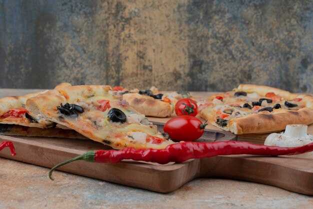 Rebanadas de pizza sobre tabla de madera con tomates cherry y ají.