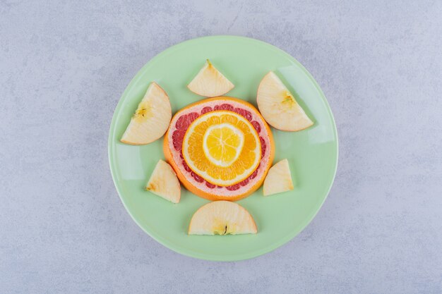 Rebanadas de pomelo fresco, naranja, limón y manzana en placa verde.