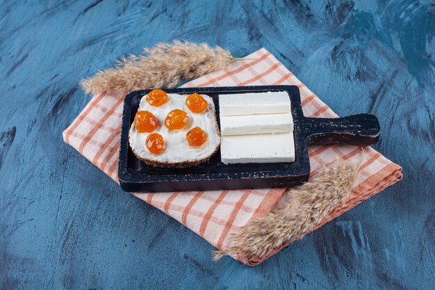 Rebanadas de queso blanco y pan con crema y mermelada en la tabla de cortar