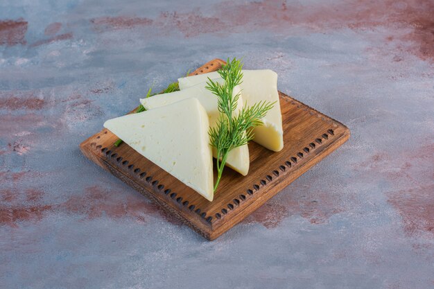 Rebanadas de queso y eneldo sobre una placa de cerca, sobre el fondo de mármol.