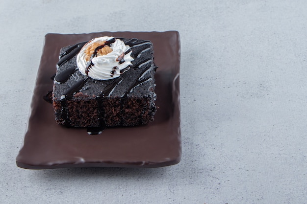 Rebanadas de sabroso brownie de chocolate con crema en un plato oscuro. Foto de alta calidad
