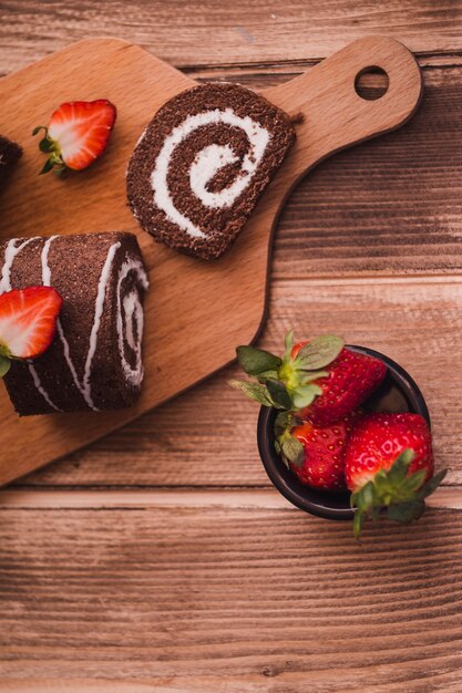 Rebanadas de sabroso rollo y fresas en la mesa de madera