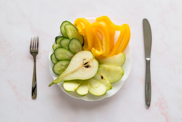 Rebanadas saludables de bellpepper; Pepino; pera en plato con tenedor y cuchillo de mantequilla